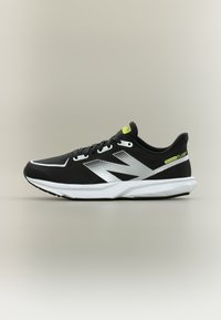 Ασπρόμαυρο αθλητικό παπούτσι New Balance με επάνω μέρος από δίχτυ, κίτρινα λογότυπα και μαλακή σόλα, εμφανιζόμενο σε πλαϊνή όψη σε μπεζ φόντο.