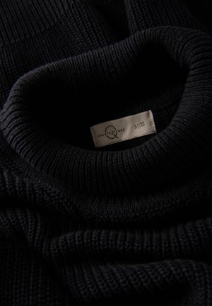 Mustassa neulepuserossa on ribbattu poolokaulus. Siinä on brändinimi sisältävä etiketti. Pehmeä rakenne ja tasaista ompelua.