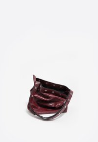 Burgundowa skórzana torba o miękkiej fakturze, luźnym fasonie i srebrnych nitach wzdłuż górnej krawędzi; posiada jeden pasek do noszenia.