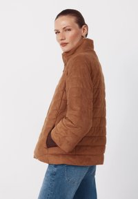 Brun quiltet jakke med høj krave, forlommer og blød tekstur, kombineret med blå denimjeans.