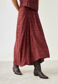 Falda larga de patrón floral rojo, hecha de una tela ligera, combinada con botines de cuero marrón que presentan detalles texturizados y tacones apilados.