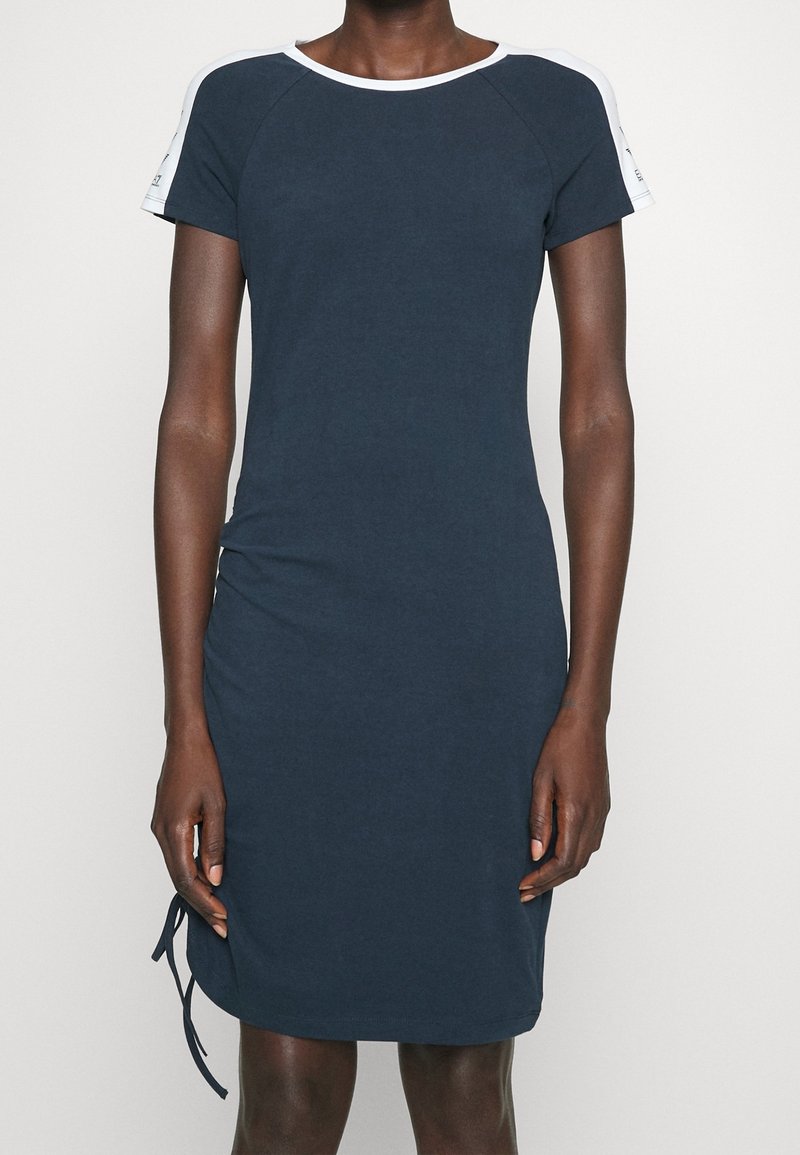 Tummanlaivansiniset lyhythihaiset mekko, jossa on pyöreä kaula-aukko ja valkoiset yksityiskohdat olkapäillä. Mekossa on sivuhauska helmassa säätömahdollisuus.