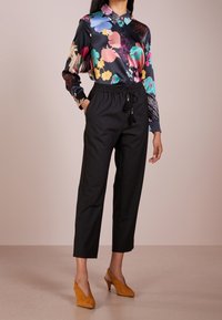 Blouse en satin à fleurs avec un col, associée à un pantalon noir fuselé avec une taille élastique. Des escarpins jaunes à bride arrière complètent le look.