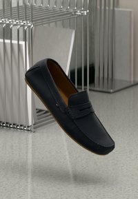 Marine læder loafers med brune gummisåler; rund tå, dekorativ syning og et frontudskæringsdetalje.