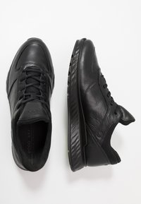 Czarne buty sportowe wykonane ze skóry i siateczki, z zaokrąglonym czubkiem, sznurowanym zapięciem oraz teksturowaną gumową podeszwą z wyraźnymi rowkami.