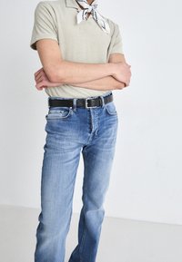 Camisa polo beige clara con cuello, jeans de mezclilla azules de corte recto, y un cinturón negro con hebilla de plata. Textura suave.