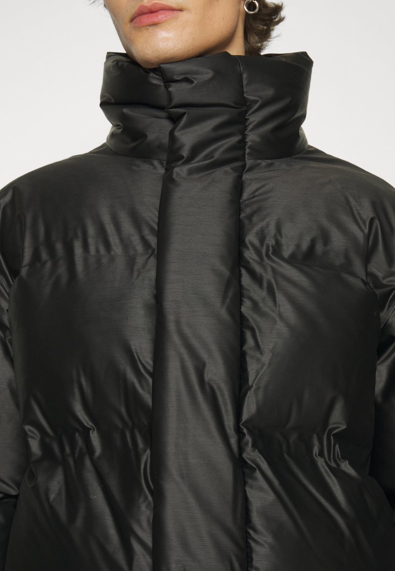 Chaqueta acolchada negra con cuello alto, textura suave, secciones acolchadas horizontales y cierre frontal superpuesto.