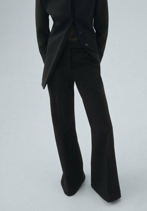 Black tailored suit jacket with a pointed hem and two buttons, paired with black wide-leg trousers, both made from a smooth fabric.