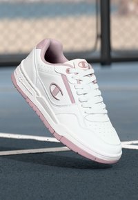 Białe sneakersy z różowymi akcentami, górna część z gładkiej skóry, perforowane palce, płaska podeszwa i sznurowana konstrukcja. Logo z boku i na języku.