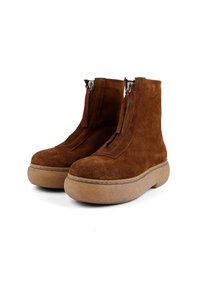 Braune Wildleder-Ankle-Boots mit abgerundetem Zeh, flacher Plateausohle und vorderen Reißverschlüssen. Das Design zeichnet sich durch sichtbare Nähte und eine weiche Textur aus.