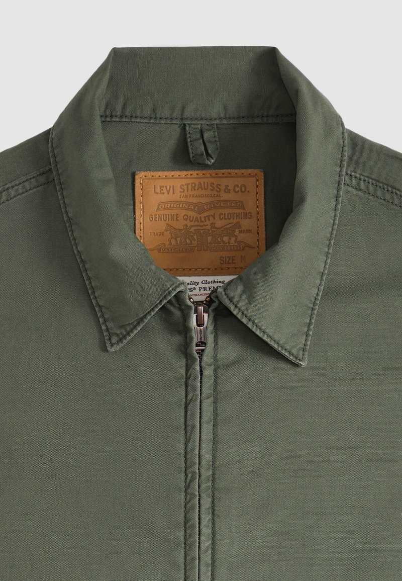 Chaqueta verde oliva con cremallera, cuello puntiagudo y etiqueta marrón Levi Strauss & Co. dentro del cuello que indica talla M.