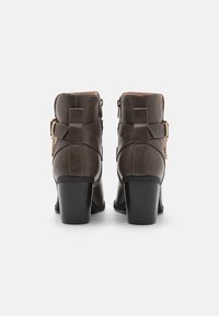Brune lær ankle boots med en rund tå, kraftig hæl og dekorative stropper. Utstyrt med gullfarget metall og en glidelås på siden.