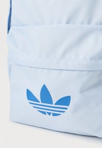 Ανοιχτό μπλε σακίδιο πλάτης από ανθεκτικό ύφασμα με λεία υφή. Διαθέτει μπλε λογότυπο Adidas με σχεδιασμό τριών ρίγων στην μπροστινή τσέπη.