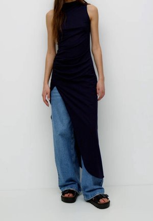 Top senza maniche blu navy con design arricciato e orlo asimmetrico, abbinato a jeans leggeri azzurri e sandali neri con plateau.