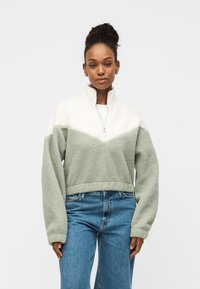 Φλίς πουλόβερ με σχεδιασμό με μπλοκ χρώματος σε λευκό και πράσινο, ψηλό γιακά και μακριά μανίκια. Υλικό με υφή απαλή, cropped εφαρμογή.