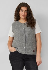 Grijze gebreide cardigan met een textuurpatroon, ronde halslijn en knoopsluiting. Gecombineerd met een wit shirt en donkere spijkerbroek.