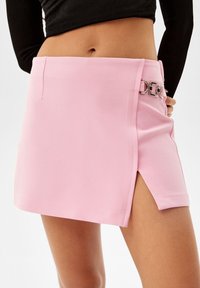 Pink mini skirt with a side slit, made of smooth fabric. Features a silver accent detail on the waistband. Straight cut design.