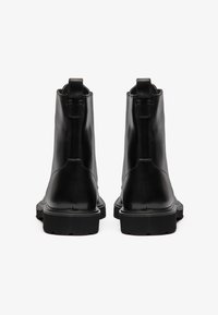 Botas de cuero negro hasta el tobillo con un acabado suave, que cuentan con una suela resistente, un diseño minimalista y tiradores en la parte trasera para facilitar su uso.