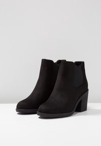 Bottines en suède noir avec panneaux latéraux élastiques, bout rond, talon texturé et couture le long de la semelle.