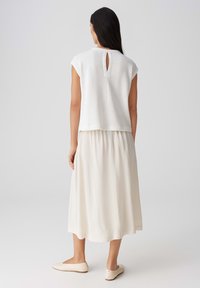 Witte top met korte mouwen van textuur gebreid, met een sleufdetail aan de achterkant. Gecombineerd met een vloeiende, lichtbeige rok en zachte, beige schoenen.