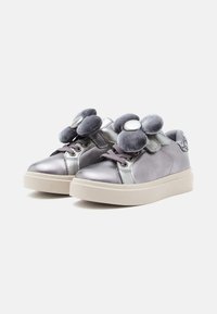 Zapatillas infantiles metálico gris con suelas blancas gruesas, cordones y grandes decoraciones de flores de tela en la parte superior.