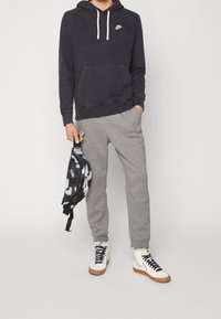 Ciemnogranatowa bluza z kapturem z białymi sznurkami i logo Nike, szare spodnie dresowe, białe trampki z granatowymi sznurowadłami oraz czarno-biała torba z wzorem.