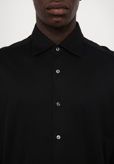 Svart skjorte med knapper og en strukturert krage, med lyse knapper og en glatt, matt tekstur. Ingen mønstre eller detaljer.