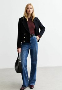 Svart dubbelframsidan kappa med guldknappar, vinröd tröja, blå vida jeans och svart handväska. Modellen bär vinröda skor.