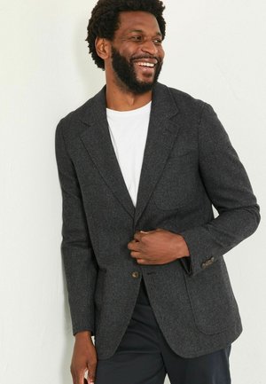 Dunkelgrau, strukturierter Blazer mit einem Knopf, Reverskragen und vorderen Taschen, getragen über einem weißen T-Shirt und schwarzen Hosen.