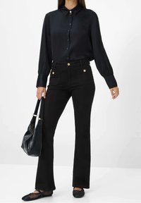 Musta satiinipaito, jossa on pitkät hihat ja napitus, yhdistettynä korkeavyötäröisiin mustiin leveälahkeisiin housuihin, joissa on kultaiset nappikoristeet.