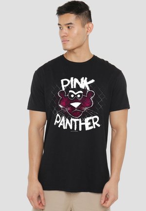 Junger Mann trägt ein schwarzes T-Shirt mit einem grafischen Druck des rosa Panthers und dem Text "Pink Panther". Er schaut nach links vor einem einfarbigen Hintergrund.