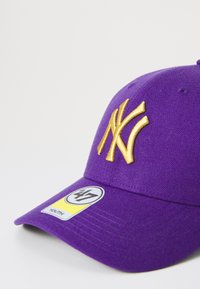 Fialová baseballová čapica s vyšitým zlatým logom "NY", vrátane žltého štítka s "47" a označením "YOUTH". Hladká textúra látky.