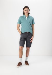 Teal polo-shirt med hvid krave, parret med grå cargo-shorts. Brune sneakers, hvide sokker. Simpelt design, behagelig pasform.