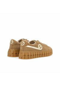 Tan suede sneakers with a chunky, textured gum sole, featuring a metallic accent on the side and logo detailing on the heel.