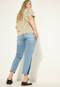 Zelený květinový top s krátkým rukávem, modré úzké džíny s postranním panelem a černé platformové boty. Texturované látky, uvolněný střih.