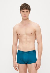 Tirkīzzili bezkokvilnas bokseršorti ar melnu Calvin Klein jostasvietu; pieskaņots dizains; gluda tekstūra; bez rakstiem vai papildu detaļām.