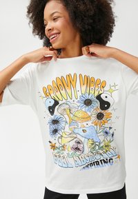 Hvid oversized T-shirt med farverig grafisk print af blomster, svampe og yin-yang symboler. Rund hals og korte ærmer.