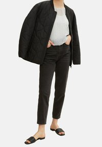 Giacca bomber trapuntata nera, top bianco a fantasia, jeans a vita alta neri e sandali neri scivolati, caratterizzati da texture morbide e design semplice.