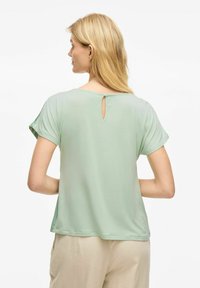 Top verde chiaro a maniche corte con dettaglio a chiave sul retro, realizzato in tessuto morbido. Vestibilità ampia con scollatura rotonda e maniche arrotolate.