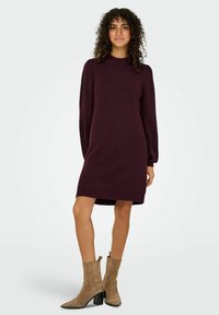 Abito a maglia bordeaux con collo alto, maniche lunghe a palloncino e silhouette dritta, abbinato a stivaletti alla caviglia in suede beige.
