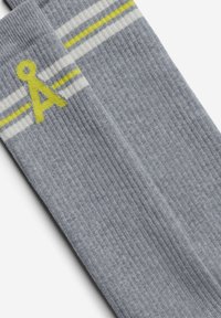 Graue Socken mit gerippter Textur, die gelbe und weiße Streifen sowie ein gelbes „A“-Design im oberen Bereich aufweisen.