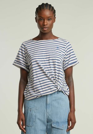 Striped t-shirt in light cream and navy, features a knotted side detail, wide neckline, and relaxed fit. Paired with light blue cargo pants.