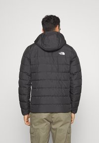 Mustat puffatakki hupulla, jossa on ommeltuja osia eristyksen lisäämiseksi, ja pieni valkoinen logo yläselässä. Yhdistetty oliivinvihreisiin cargo-housuihin.