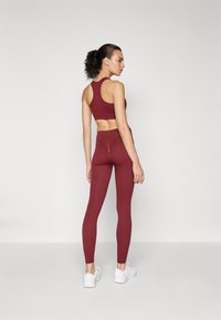 Un sutien sport bordeaux cu un design tip racerback, asociat cu leggings cu talie înaltă, asortați. Ambele piese sunt fabricate dintr-un material elastic, texturat.