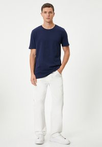 Marinblå kortärmad T-shirt i kombination med vita cargobyxor och vita sneakers. T-shirten har rundad halsringning och en avslappnad passform.