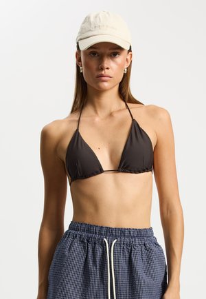 Czarny trójkątny top od bikini z cienkimi ramiączkami; zestawiony z luźnymi niebieskimi szortami w kratę z troczkiem. Kremowa czapka z daszkiem.