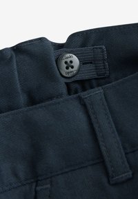 Marineblauwe broek van een gestructureerde stof, met een knoopsluiting met het Clarks-logo en lussen voor de riem langs de tailleband.
