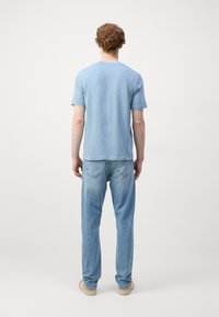 Světle modré bavlněné tričko s krátkým rukávem, volný střih. V kombinaci s vybledlými světle modrými džíny. Jednoduchý design, minimální detaily na textuře látky.
