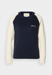 Pull col rond bleu marine avec manches raglan longues blanches et "Gant 1949" brodé sur le côté gauche de la poitrine.