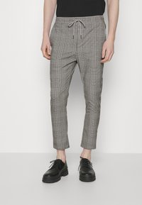 Geruit zwart-wit broek met een trekkoord in de taille, slim fit, taps toelopende pijpen en enkel lengte, gedragen met zwarte veterschoenen.